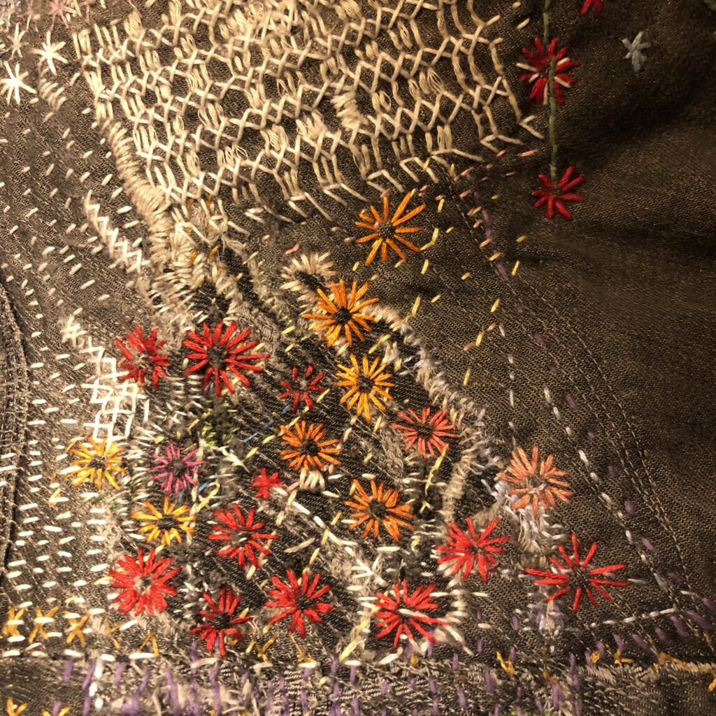 Visibly mended jeans, a bit with white/light criss-crossing lines and red/orange stitched flowers atop.