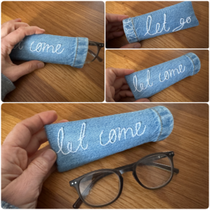 A handmade denim case for reading glasses, embroidered with 'Let go, let come'.